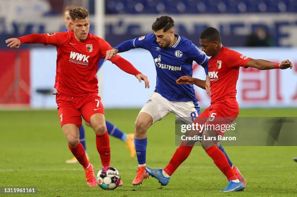 Suat Serdar of FC Schalke 04 battles for possession with Florian Niederlechner and Carlos Gruezo of FC Augsburg during the Bundesliga match between...