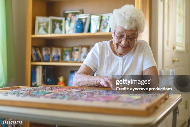 elderly woman at home working on jigsaw puzzle active senior photo series - puzzle imagens e fotografias de stock