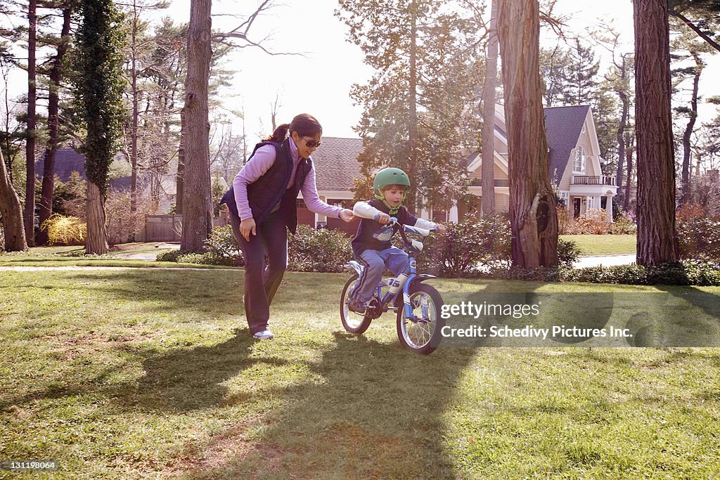 Mom teaches her son to ride a bicycle on lawn