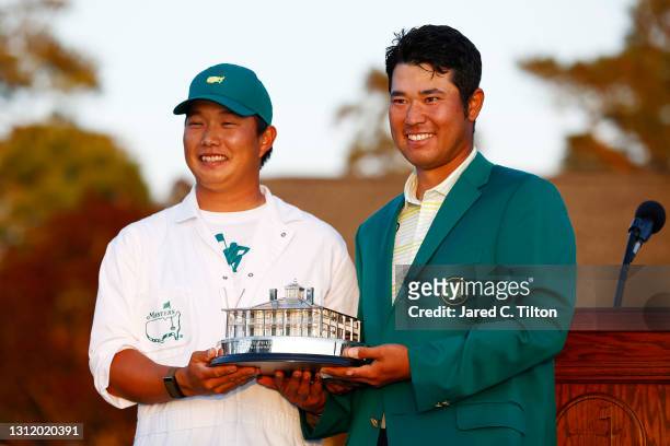 Hideki Matsuyama of Japan poses with his caddie, Shota Hayafuji, and the Masters Trophy during the Green Jacket Ceremony after winning the Masters at...