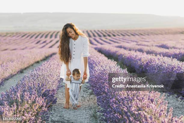 mom and baby daughter having fun laughing and walking in lavender field - baby lachen natur stock-fotos und bilder