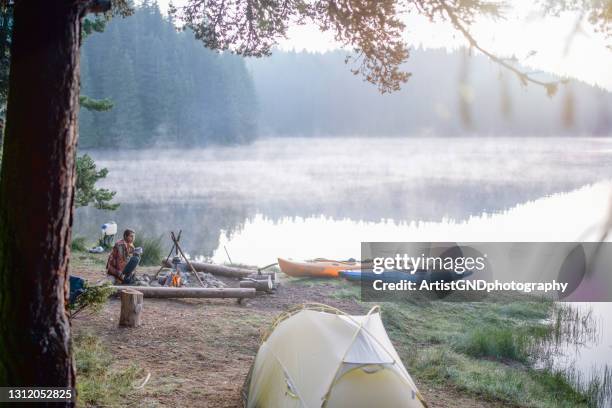 portrait of a young beautiful woman sitting next to campfire and enjoying herbal tea in the morning. - summer camp canoe stock pictures, royalty-free photos & images