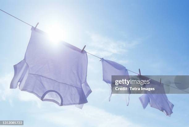 low angle view of laundry drying on clothesline against sky and sun - frische stock-fotos und bilder