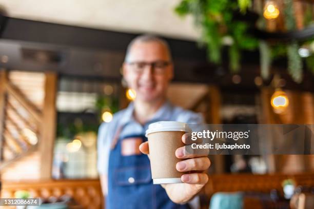 cameriere maturo che tiene e serve una tazza di carta di caffè caldo - tazzina di carta foto e immagini stock