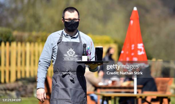 Man wearing a mask serves drinks whilst in a beer garden at Hotel Rudyard on April 12, 2021 in Leek, England. England has taken a significant step in...