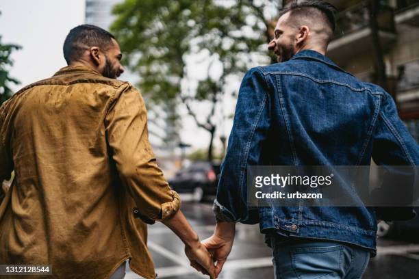 pareja gay caminando bajo la lluvia tomado de la mano - hombre gay fotografías e imágenes de stock