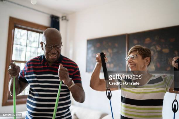 senior couple exercising with resistance band at home - active retirement community stock pictures, royalty-free photos & images