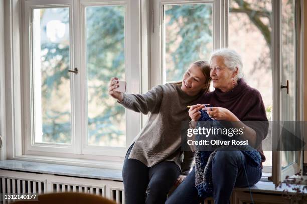 grandmother and adult granddaughter taking a selfie on windowsill - old granny knitting stock-fotos und bilder