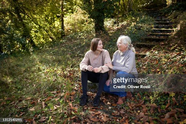 grandmother and adult granddaughter sitting in autumnal garden - nur erwachsene stock-fotos und bilder