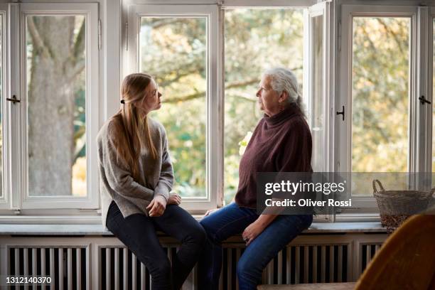 grandmother and adult granddaughter sitting on windowsill - young woman with grandmother stock pictures, royalty-free photos & images