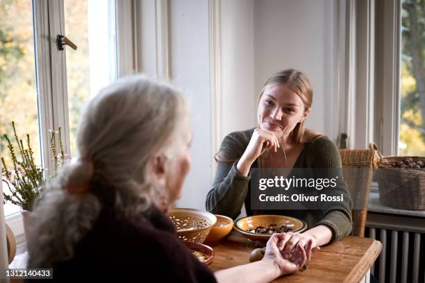 grandmother and adult granddaughter holding hands at table - granny stockfoto's en -beelden