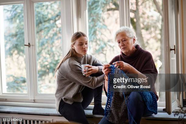 granddaughter watching senior woman knitting on windowsill - masche stock-fotos und bilder