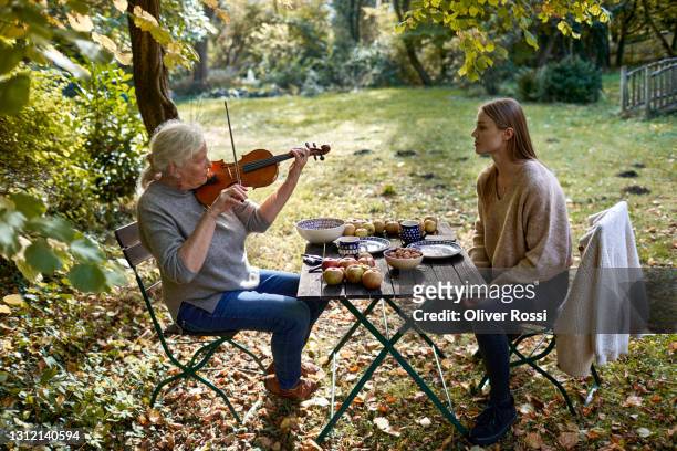 senior woman with granddaughter playing violin in garden - violin family stock pictures, royalty-free photos & images