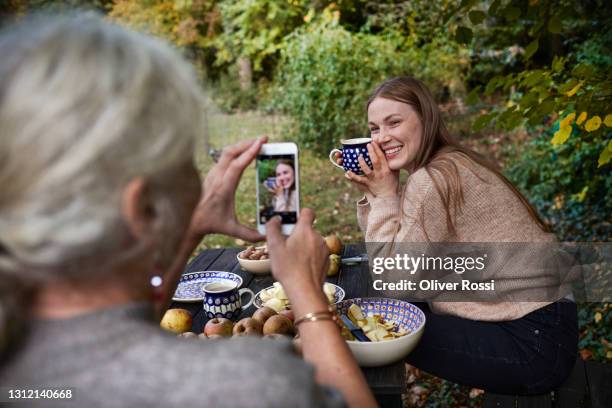 grandmother taking smartphone picture of adult granddaughter in garden - memorial garden stock pictures, royalty-free photos & images