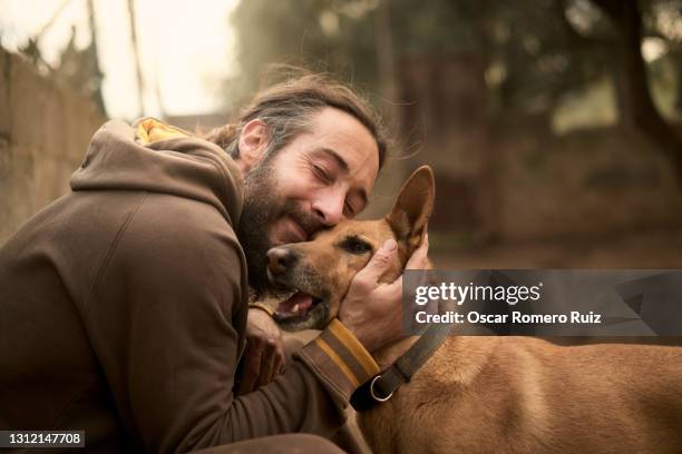 young bearded adult man hugging his dog - homme content chez lui photos et images de collection