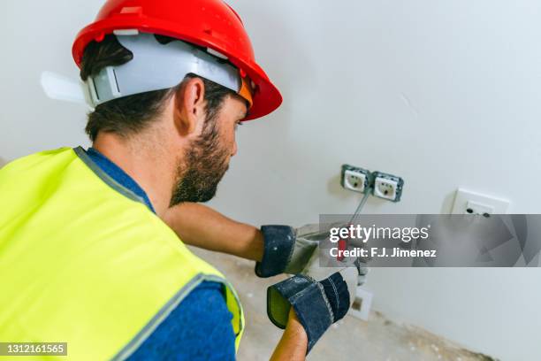 electrician on the construction site putting plug - toma eléctrica fotografías e imágenes de stock