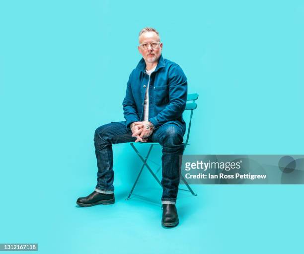 middle-aged man sitting on chair in studio - ganzkörperansicht stock-fotos und bilder