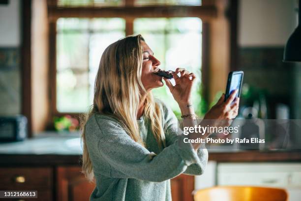 woman eating pie in the kitchen while doing video call - blonde woman selfie foto e immagini stock