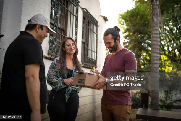 male courier delivering package to couple at home - receiving delivery stock pictures, royalty-free photos & images