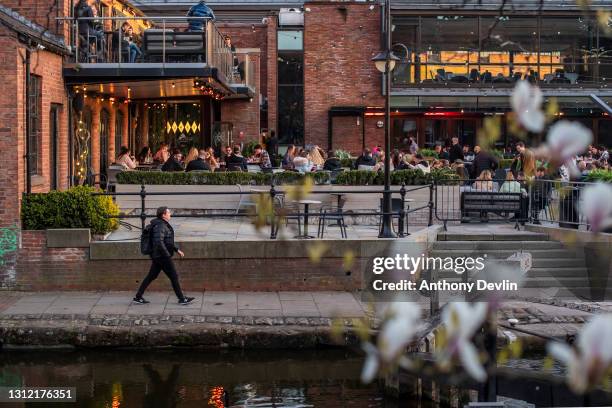 Man walks along the Rochdale canal as patrons sit in the beer garden at Dukes 92 bar on April 12, 2021 in Manchester, England. England has taken a...