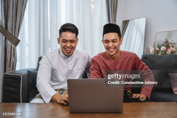 celebrating hari raya virtually. young men wearing malay traditional costume making online video call on laptop. - malayan ethnicity stock pictures, royalty-free photos & images