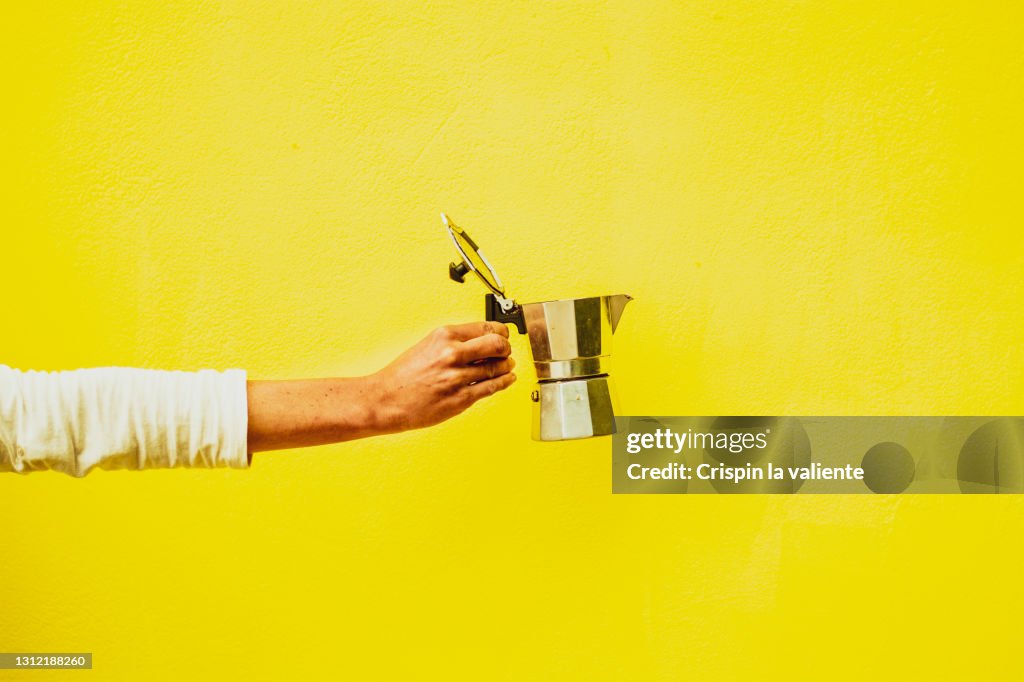 Woman hand holding italian coffee pot with lid open with yellow background
