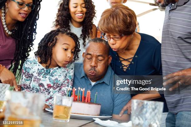 senior couple blowing birthday candles during party with family - senior birthday stock pictures, royalty-free photos & images