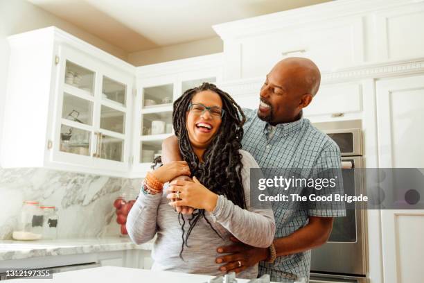 smiling man embracing female partner in kitchen at home - woman couple at home stockfoto's en -beelden