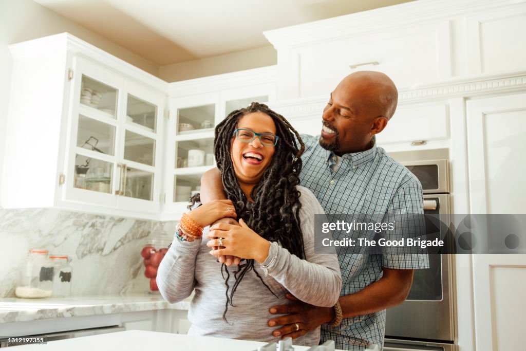 Smiling man embracing female partner in kitchen at home
