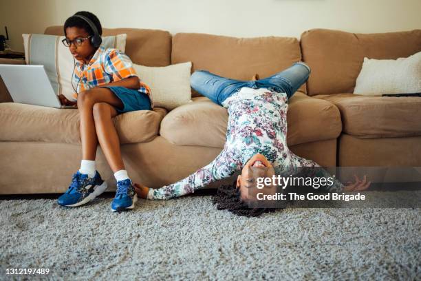 portrait of smiling girl on sofa while boy using laptop in living room - living room kids stockfoto's en -beelden