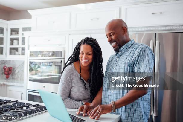 man and woman using laptop in kitchen at home - man 45 stock pictures, royalty-free photos & images