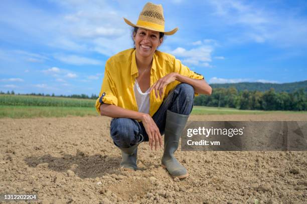 smiling hispanic adult woman crouching on brown leveled field. - leveled stock pictures, royalty-free photos & images