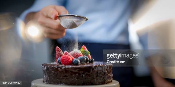 man finishing tasty multi-tier cake. male hand holding strainer and sprinkling top of cake with icing sugar. - finishing cake stock pictures, royalty-free photos & images