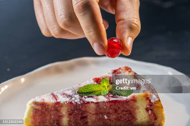 close-up of male hand adding candied cherry on piece of cake. - fruit pie stock pictures, royalty-free photos & images