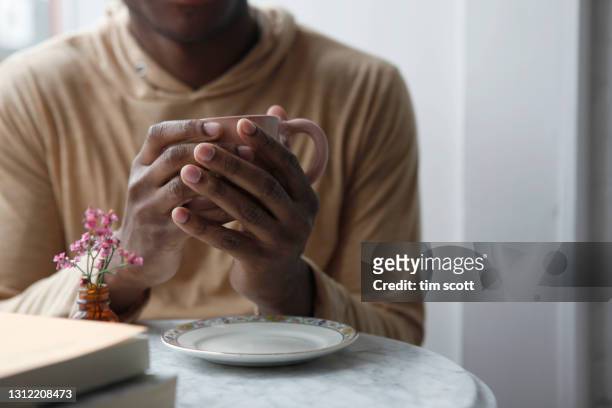 close-up of a man's hand holding a coffee cup at a table in a cafe - black cup saucer stock pictures, royalty-free photos & images
