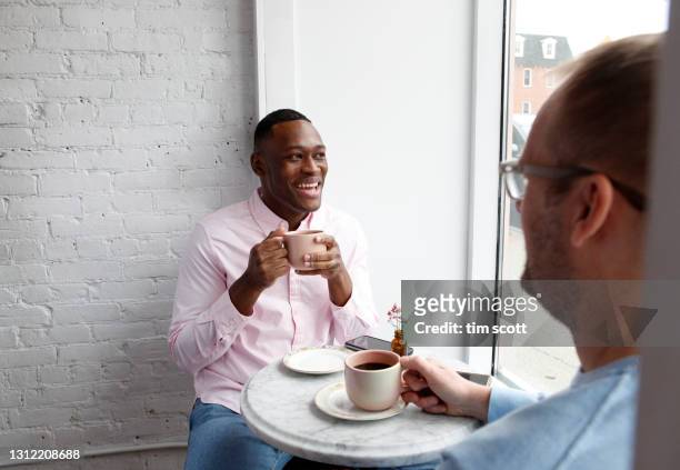 man sitting at cafe table with a cup of coffee, smiling at another man - fancy coffee drink stock pictures, royalty-free photos & images