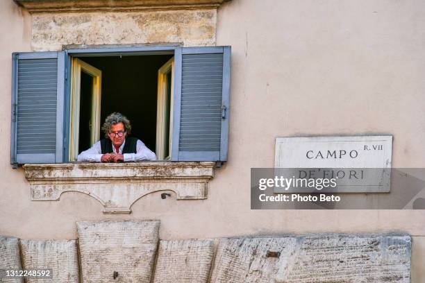 a man looks out of a window in the square of campo de fiori in the historic heart of rome - campo de fiori stock pictures, royalty-free photos & images