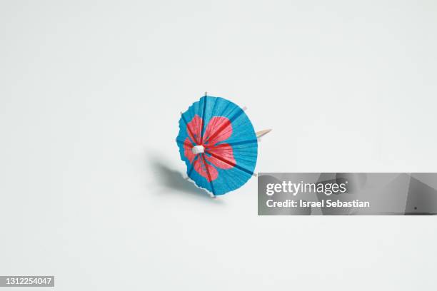 image from above of colorful cocktail paper umbrella with soft shadows on white background.  summer weather concept - drink umbrella stock pictures, royalty-free photos & images