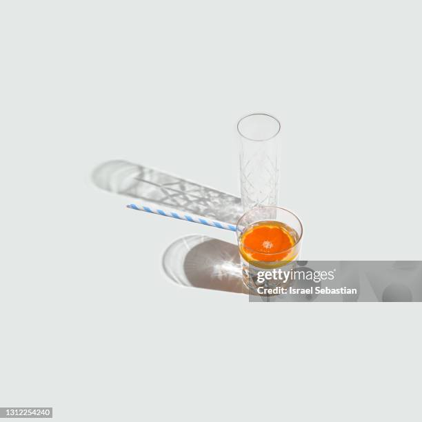 from the top a pair of crystal glasses one filled with very cold water with a slice of blood orange and another empty tube glass on a white background. refreshing drink for the summer. - alcohol detox foto e immagini stock