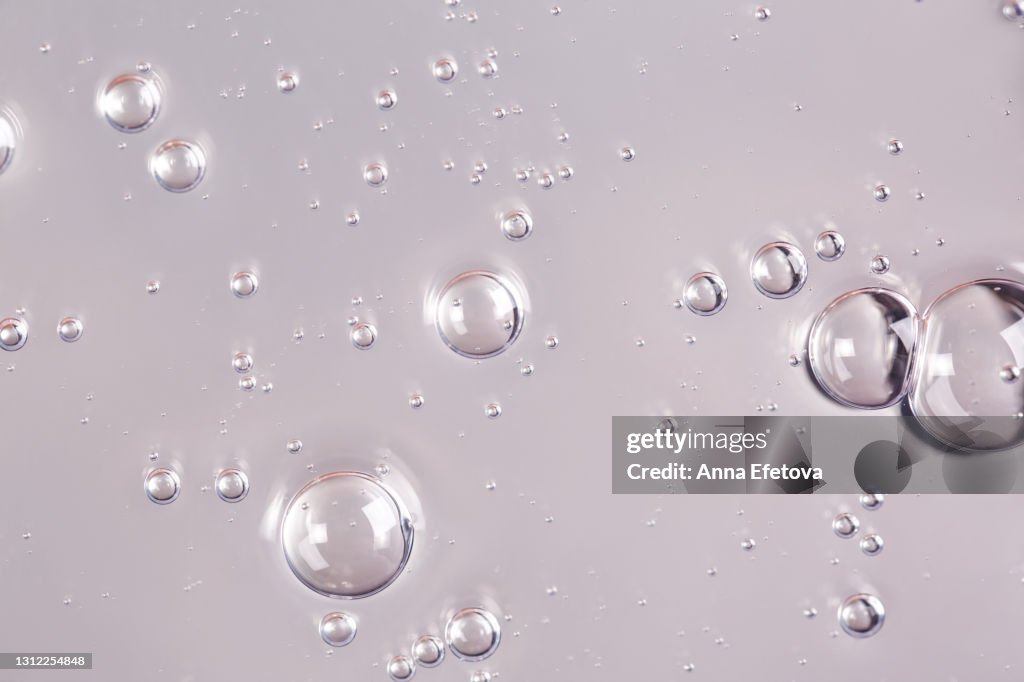 Texture of organic transparent gel with many air bubbles smudged on ultimate gray silver monochrome background. Concept of skin moisturizing or prevention Covid-19 during pandemic. Trendy colors of the year 2021. Close-up and flat lay style