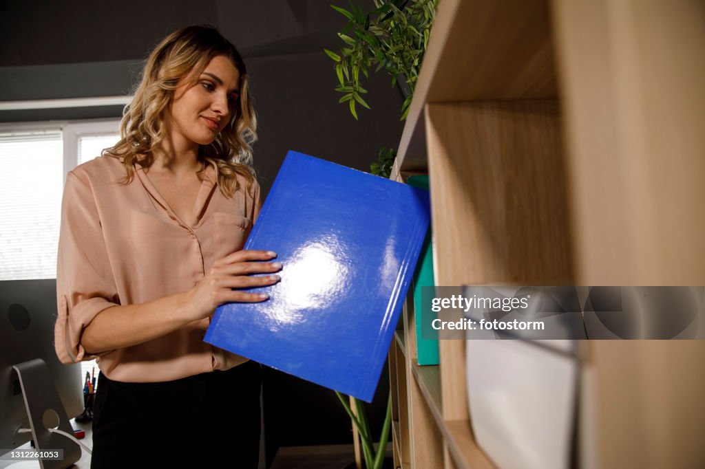 Smiling businesswoman checking files and documents on the shelf at the office