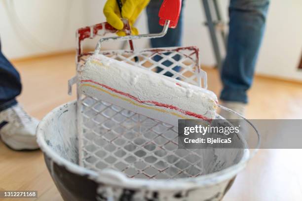 woman dipping paint roller in bucket with white paint while painting interior walls with her husband at home - paint tray stock pictures, royalty-free photos & images