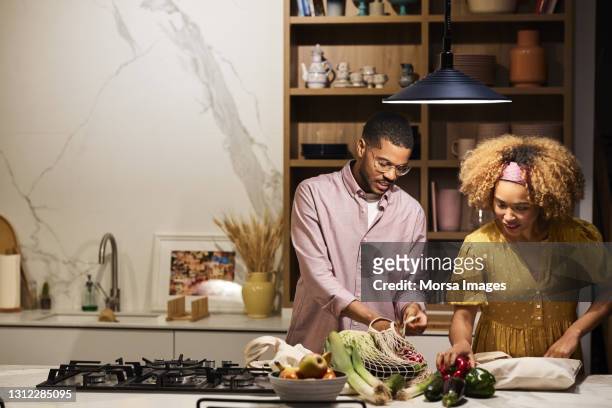 smiling couple with vegetables at kitchen island - young man groceries kitchen stock pictures, royalty-free photos & images