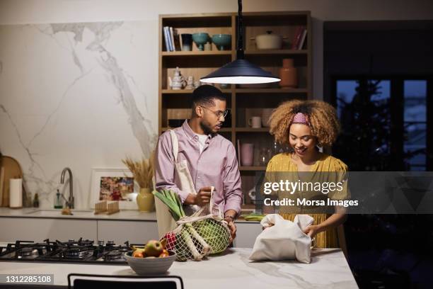 man looking at afro girlfriend with groceries - young man groceries kitchen stock-fotos und bilder