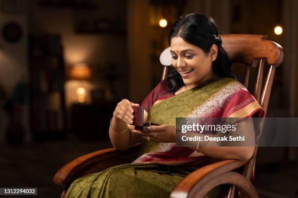 shot of a woman in sari got shocked while opening the diamond box of ring sitting on a rocking chair at home:- stock photo - gold jewellery india stock pictures, royalty-free photos & images