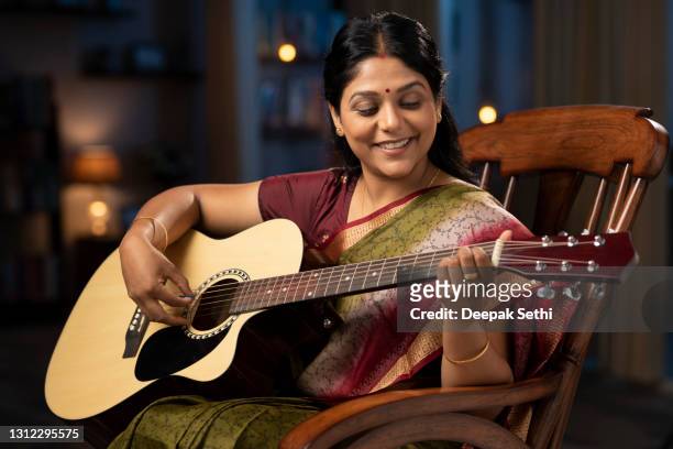 shot of a woman in sari playing guitar sitting on a rocking chair at home:- stock photo - musician stock pictures, royalty-free photos & images