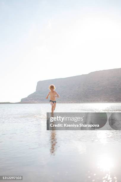 a boy runs through the water during sunset. balos beach and paradise island in crete, greece-stock photo - balonnen stock-fotos und bilder