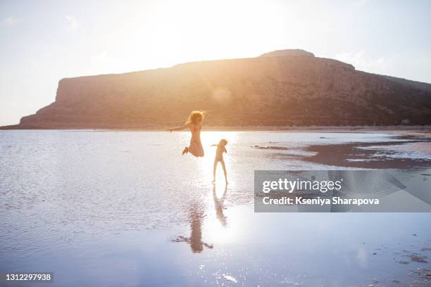 a boy and a woman jump into the sea at sunset.beauty of balos beach and paradise island in crete, greece-stock photo - balonnen stock-fotos und bilder
