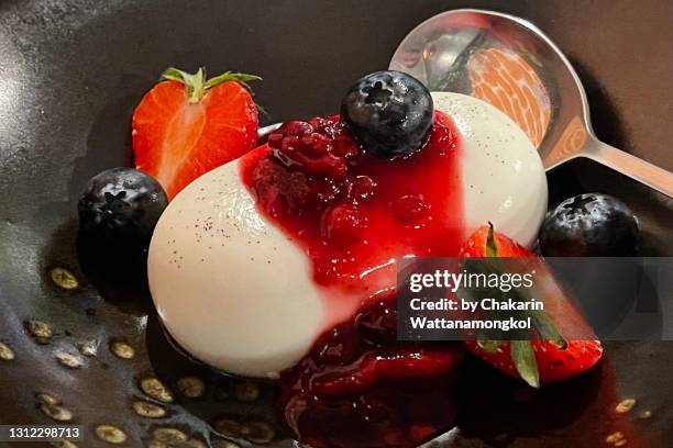 panna cotta with strawberry sauce served on black plate. - strawberries and cream stock-fotos und bilder