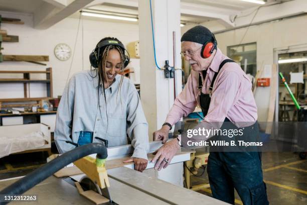 technician showing young intern how to use table saw - handwerker stock-fotos und bilder
